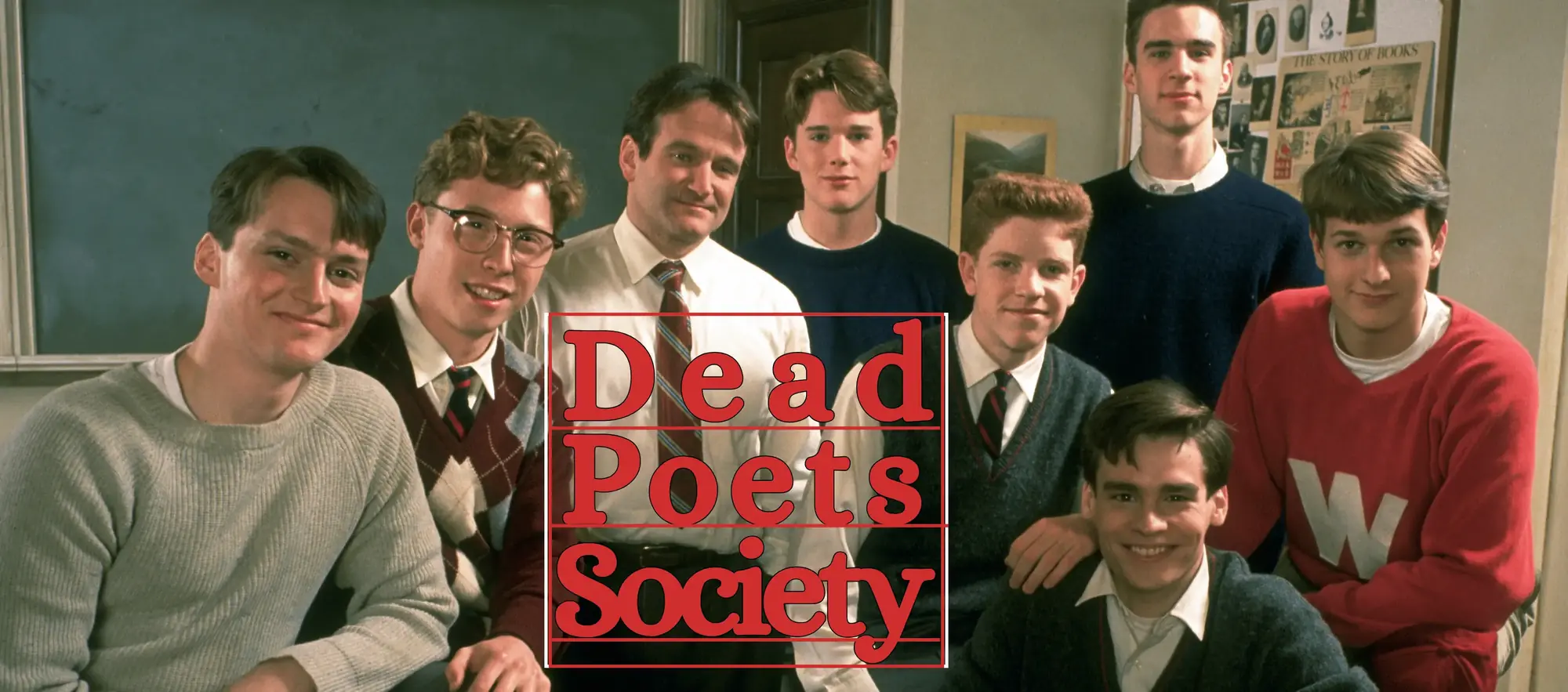 A ensemble group portrait featuring eight cast members from the 1989 film Dead Poets Society inside a classic classroom setting. At the center stands Robin Williams as John Keating, wearing a white button-down shirt, dark tie, and trousers, surrounded by his students who wear preppy late-1950s boarding school attire including sweater vests, knit jumpers, collared shirts, and neckties in shades of gray, navy, maroon, and red. Surrounding Keating are the core cast members including Ethan Hawke, Robert Sean Leonard, Josh Charles, Gale Hansen, Dylan Kussman, Allelon Ruggiero, and James Waterston, all looking directly at the camera with gentle, warm smiles. The background shows a dimly lit classroom with a chalkboard, wood panelling, and a notice board pinned with historical documents. Red serif typography reading "Dead Poets Society" is overlaid prominently across the lower center of the frame.