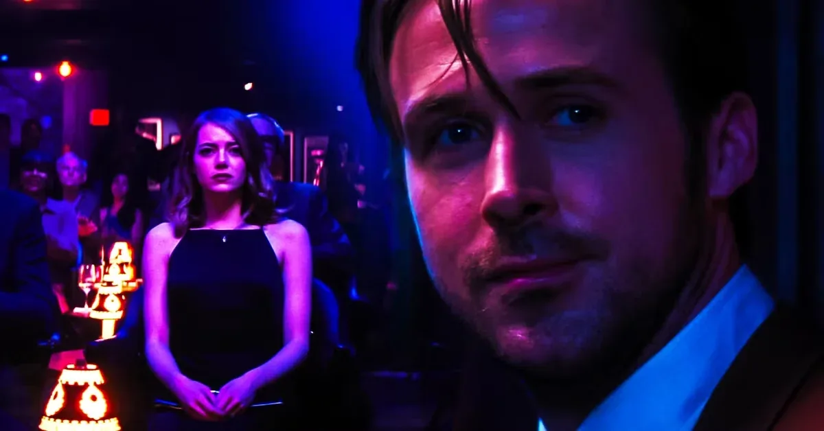 An extreme close-up focuses on a light-skinned man with dark hair, a mustache, and a short beard, wearing a white collared shirt under a dark suit jacket, his expression a mix of longing and sadness. His face is lit with vibrant purple and pink hues, casting deep shadows on the right side of his face. In the blurred background, a light-skinned woman with shoulder-length brown hair wearing a black halter-neck dress stands under a stark spotlight, looking toward the man with a somber expression. She is surrounded by a dimly lit crowd of seated people in a theater setting, with small lamps illuminating their tables with warm orange light.